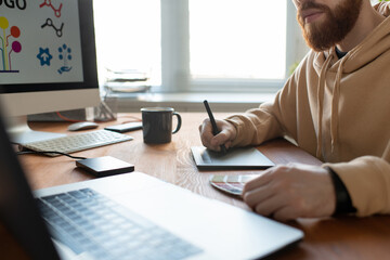 Wall Mural - Close-up of busy brand designer sitting at desk and creating graphic design using digitizer and color palette