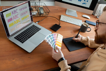 Wall Mural - Concentrated male designer writing text on drawing pad and choosing color of font