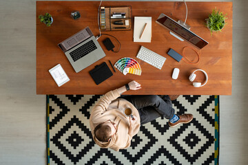 Wall Mural - Above view of relaxed designer in glasses sitting at desk with design devices and drinking coffee
