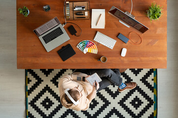 Wall Mural - Above view of modern hipster designer in headphones using digital tablet while working on scheme in home office