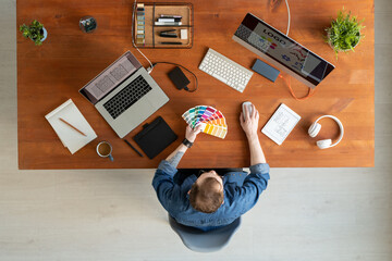 Wall Mural - Above view of young man in denim shirt choosing color on swatch while working on brand identity for company