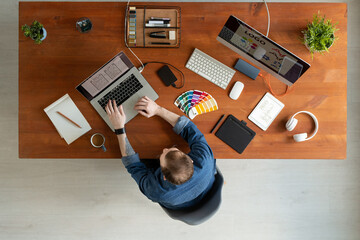 Wall Mural - Directly above view of man with tattoo sitting at wooden table and editing ui design on laptop