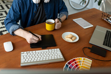 Wall Mural - Close-up of unrecognizable graphic artist sitting at wooden desk and using digitizer while creating layout