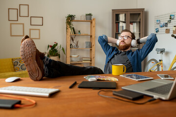 Wall Mural - Dreamy young bearded man sitting in relaxed position and listening to music in headphones while thinking of new design project