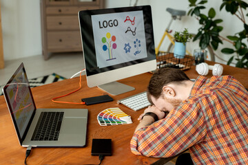 Wall Mural - Overworked designer sleeping at workplace with modern computers and hard drives