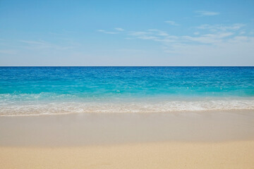 Soft ocean wave with foam licking the beautiful golden sandy beach shore. Close up of turquoise clear sea water texture on a windless and sunny summer day. Tropical background, copy space, top view.