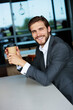 © Sergey - Charming young bearded businessman smiling, holding a paper cup of coffee