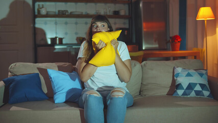 Young woman watching horror movie sitting on couch in living room at night