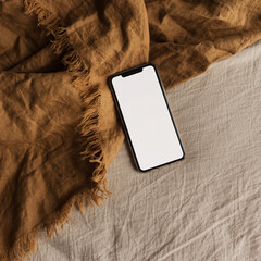 Wall Mural - Blank screen mobile phone on brown, beige blanket. Flat lay, top view. Copy space mockup template.