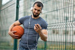 © Vladimir - Man holds a basketball in his hand, looks at a smartphone and listens to music with headphones on the street