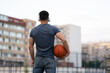 © Vladimir - Man stands with his back against the background of the city and holds a basketball in his hands