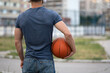 © Vladimir - Man stands with his back against the background of the city and holds a basketball in his hands close up