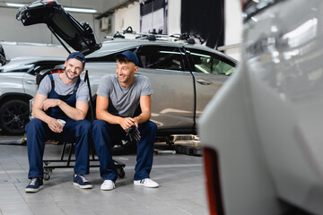 Wall Mural - Selective focus of happy auto mechanics sitting and holding paper cup and latex gloves at service station