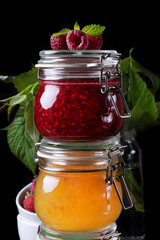 Wall Mural - Raspberry and orange jams in glass jars against the black background