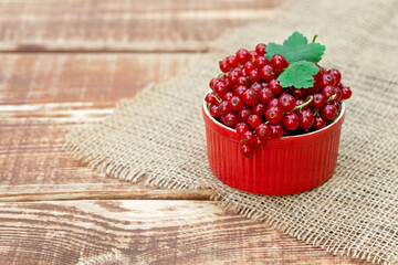 Wall Mural - Red currant berries in a cocotte bowl on a wooden background with burlap. Natural vitamins concept.