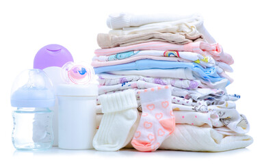 Stack folded baby clothes, soother, bottle for feeding, lotion cream for body baby on white background isolation