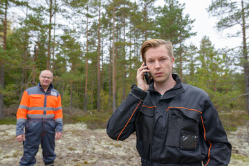 Young man talking on mobile phone in the forest with happy mature man in the background