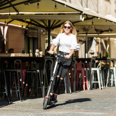 Wall Mural - Trendy fashinable teenager girls riding public rental electric scooters in urban city environment. New eco-friendly modern public city transport in Ljubljana, Slovenia.