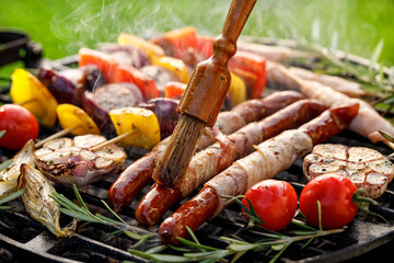 Wall Mural - Grilled food, spreading aromatic marinade of bacon wrapped sausages close up view