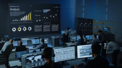 Wall Mural - Static Shot of Professional Traders Working in a Modern Monitoring Office with Live Analytics Feed on a Big Digital Screen. Monitoring Room Brokers and Finance Specialists Sit in Front of Computers. 