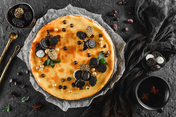 Wall Mural - Classic cheesecake with caramel, mini oreos, mint leaves, and berries on paper over dark background, top view. Delecious sweets and dessert