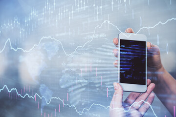 Double exposure of forex graph sketch hologram and woman holding and using a mobile device. Stock market concept.