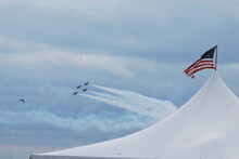 Four Of The U.S. Navy Blue Angels Flight Demonstration Squadron Speed Past A Tent With The American Flag. 
