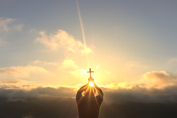 Human praying to the GOD while holding a crucifix symbol with bright sunbeam on the sky