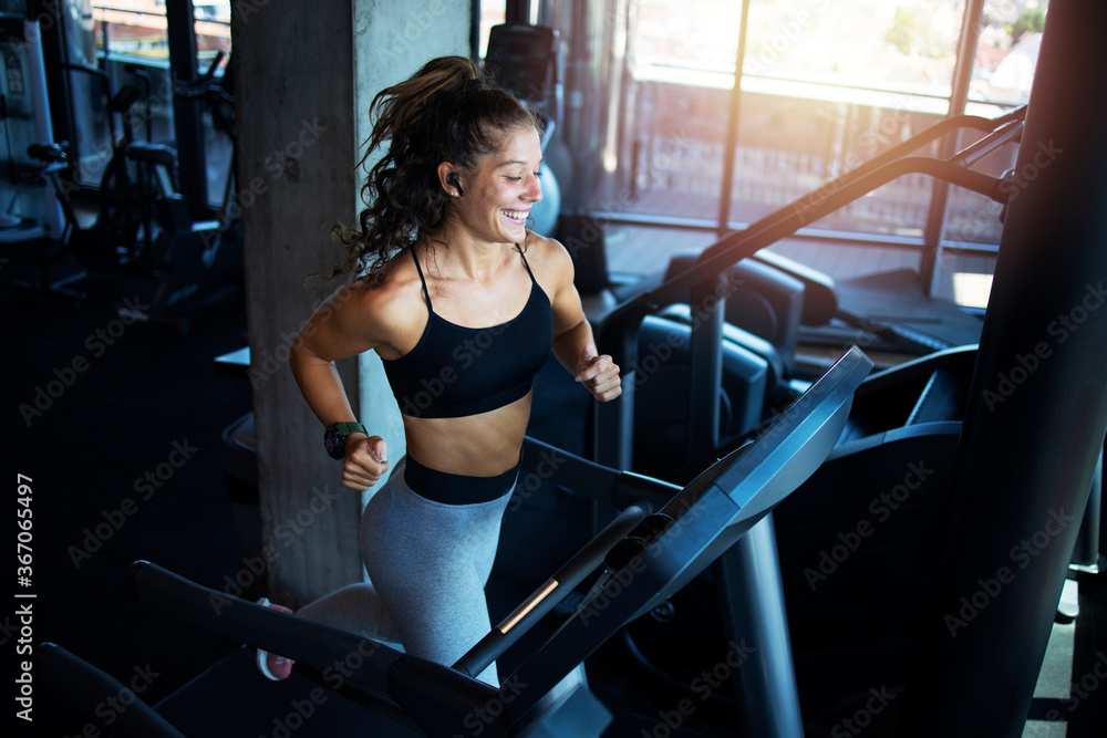 Top view of smiling woman exercising and training in the gym on treadmill running machine. Healthy lifestyle and positive people. - obrazy, fototapety, plakaty 