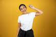 Young pretty girl holding a key with her rigth hand on yellow background looking at the front. Very happy, wearing white t-shirt and black shorts.