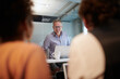 © Marc Zimmermann - Smiling businessman looking at colleagues through glass shield working in creative office during COVID-19