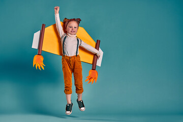 Little child girl with jet cardboard wings is playing and dreaming of becoming a pilot.