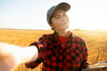 Poster - Woman farmer with digital tablet makes selfie on the background of a wheat field.	