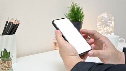 Side view of man’s hand holding smartphone on white table in home office with coffee cup, keyboard, lightbulb and blank screen smartphone. concept work from home