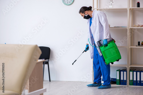 Cuadros en Lienzo Young male contractor disinfecting clinic in pandemic concept