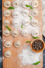 Wall Mural - Uncooked raw homemade dumplings and basil leaf on wooden board. Russian home cooking dish