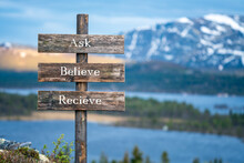 Ask Believe Recieve Ext On Wooden Signpost Outdoors In Landscape Scenery During Blue Hour. Sunset Light, Lake And Snow Capped Mountains In The Back.