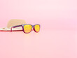 summer accessories concept from sunglasses, straw hat on pastel pink background.
