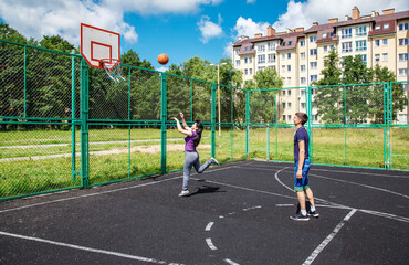 young man playing basketball with his mother on the sports ground