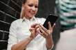 © dusanpetkovic1 - Smiling beautiful fashionable businesswoman standing outdoors and using smart phone. Business center exterior. Selective focus on the hand.