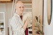 Warm-toned portrait of bald adult woman looking at camera holding wig while standing by mirror in modern home interior, alopecia and cancer awareness, copy space