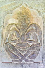 Carved Bas Relief of praying man sitting with his legs crossed,  in Angkor Wat in Siem Reap, Cambodia