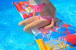 close-up - a girl in a pink swimsuit sits on a bright inflatable mattress in the pool