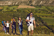 © Studio Romantic - A group of friends with backpacks on a hike in nature. Young people tourists are walking on a hill in the mountains.