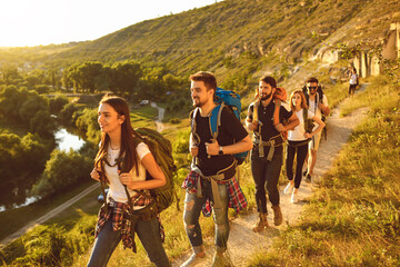 Wall Mural - young people with backpacks walking along narrow path in mountains. group of cheerful tourists hikin