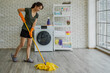 Young Asian woman cleaning floor with mop in laundry room.