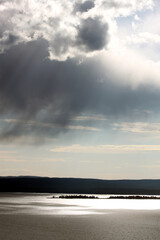 Wall Mural - Dynamic cloudy blue skies over mountains, grassy fields, and calm water