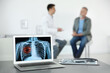© New Africa - Doctor consulting man in clinic, blurred view. Focus on laptop displaying x-ray of patient with lung cancer