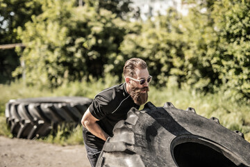 Full length side view of young man athlete flipping large tire outside gym