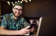 © mykolastock - Happy male hipster in earphones using laptop and smartphone looking at the camera and smiling